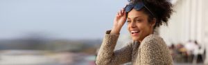 Woman smiling and holding her sunglasses against her forehead with her hand