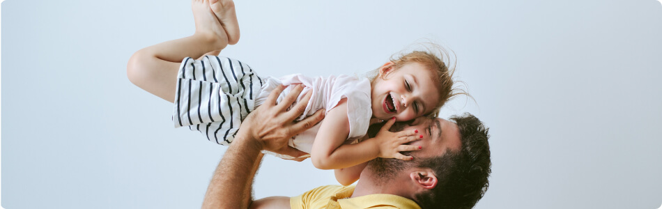 A dad kissing his daughter on the cheek while holding her up in the air