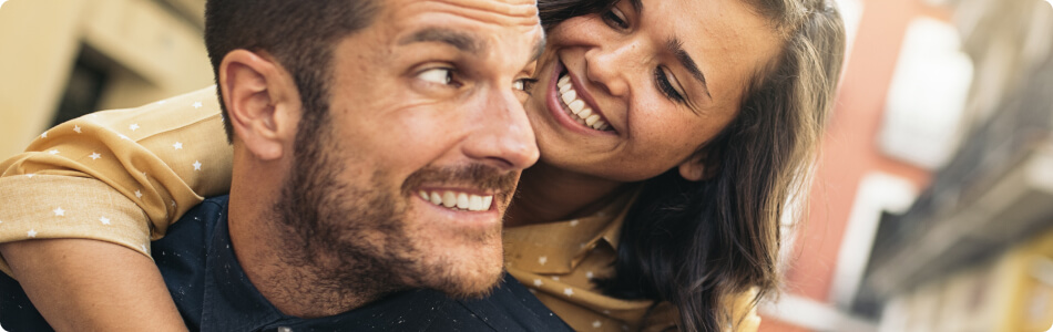 Young couple smiling at each other while man carries woman on his back