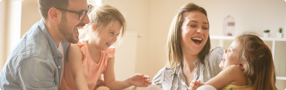 A dad, mom, and two little girls laughing together