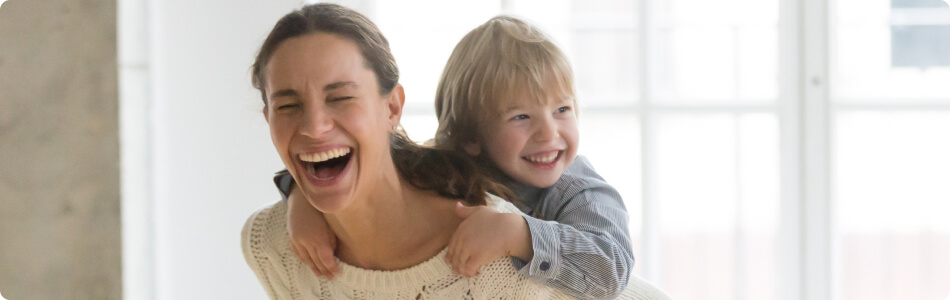 Mom laughing and carrying her little boy on her back