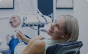 Smiling woman sitting on dentist chair, holding a mirror and looking back towards the camera