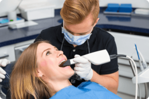 woman laying in a dentist chair while the dentist uses a laser in her mouth