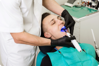man laying in a dentist chair while the dentist uses a laser in his mouth