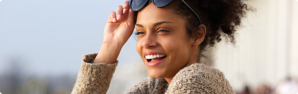 a beautiful young woman smiling outside and holding her sunglasses on her head