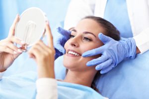 woman looking in handheld mirror in dentist chair 